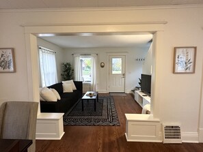 A living room with a black sofa, a coffee table, and a TV. There is a door leading to another room. - Loung Room Retreat - 3 Blocks to Mayo Campus (Rochester)
