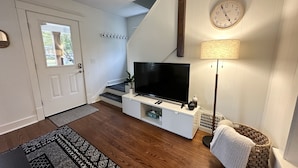 A living room with a TV, staircase, and a clock on the wall. - Loung Room Retreat - 3 Blocks to Mayo Campus (Rochester)