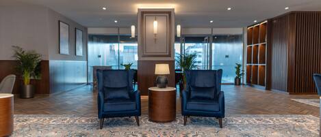 A lobby with two blue armchairs, a wooden sideboard, and a patterned carpet.