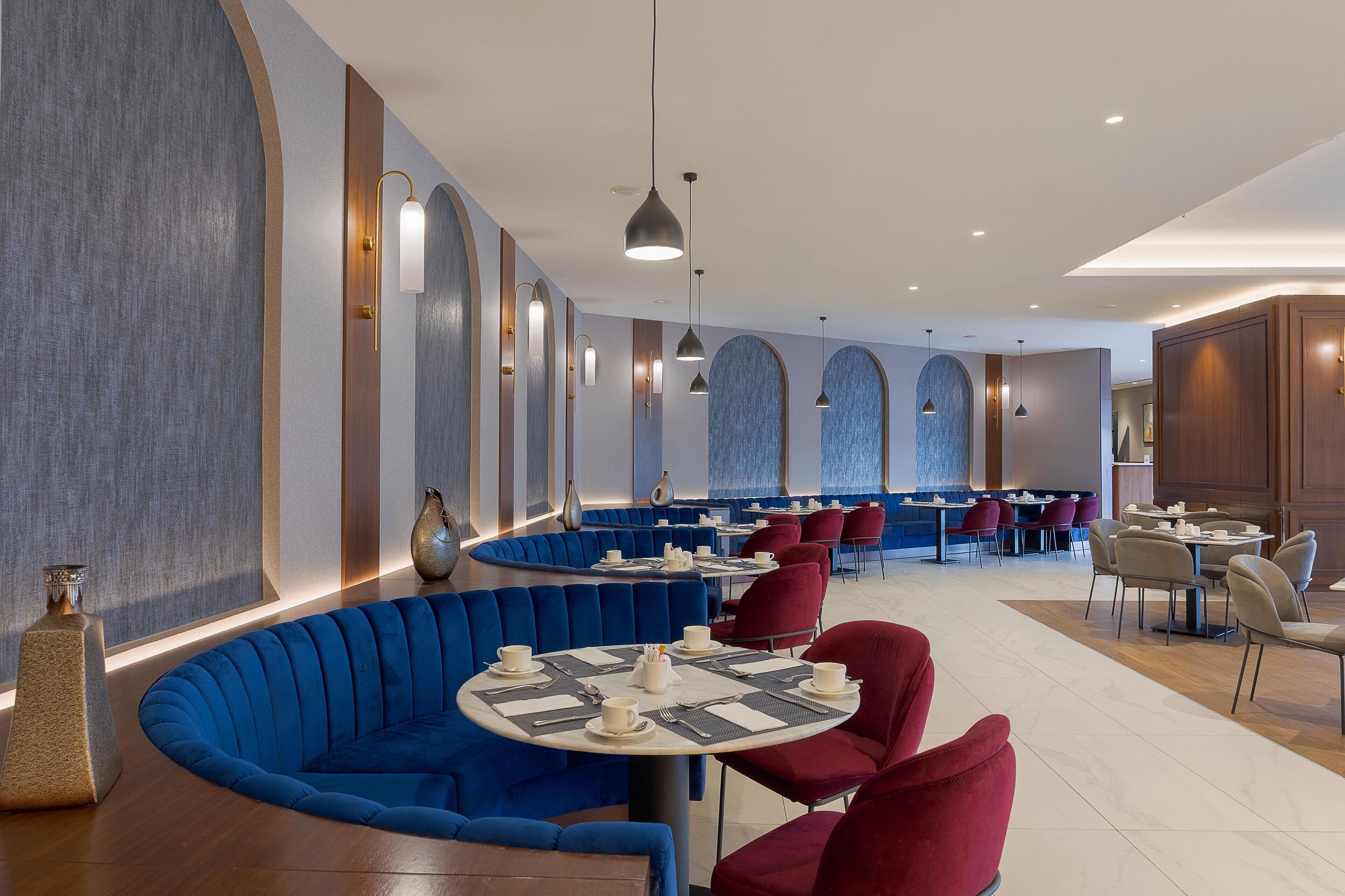 Un ristorante moderno con sedute blu, tavoli rotondi e illuminazione a sospensione.