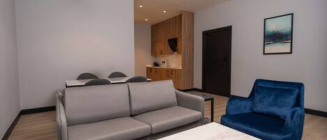 Una sala de estar moderna con un sofá gris, un sillón azul, una mesa de centro de mármol y un comedor con sillas.