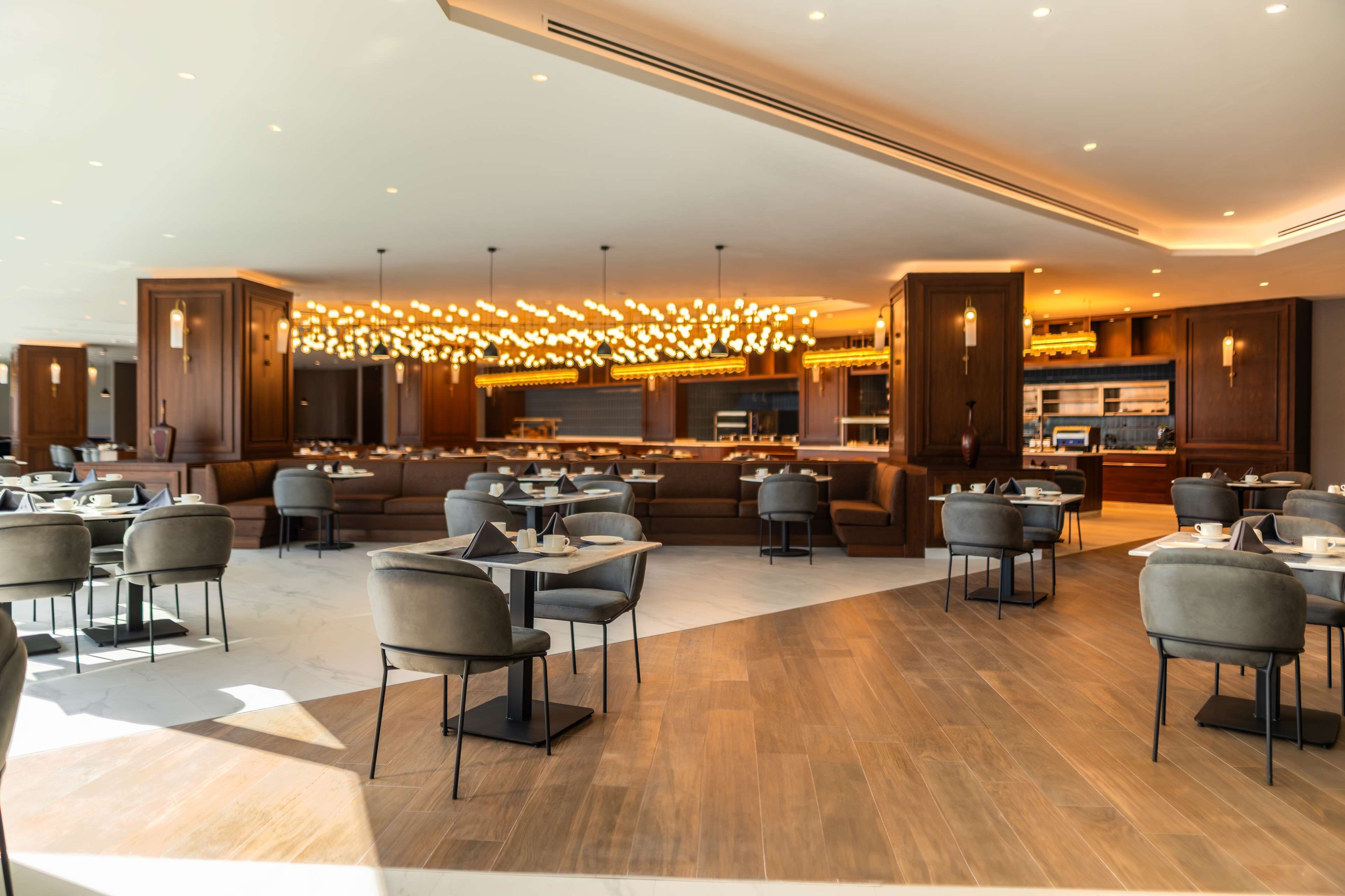 A modern restaurant with multiple seating areas, including tables and booths, and a bar area with a unique light fixture.