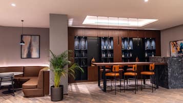 A modern bar area with a wooden bar counter, multiple shelves of bottles, and a seating arrangement with chairs.