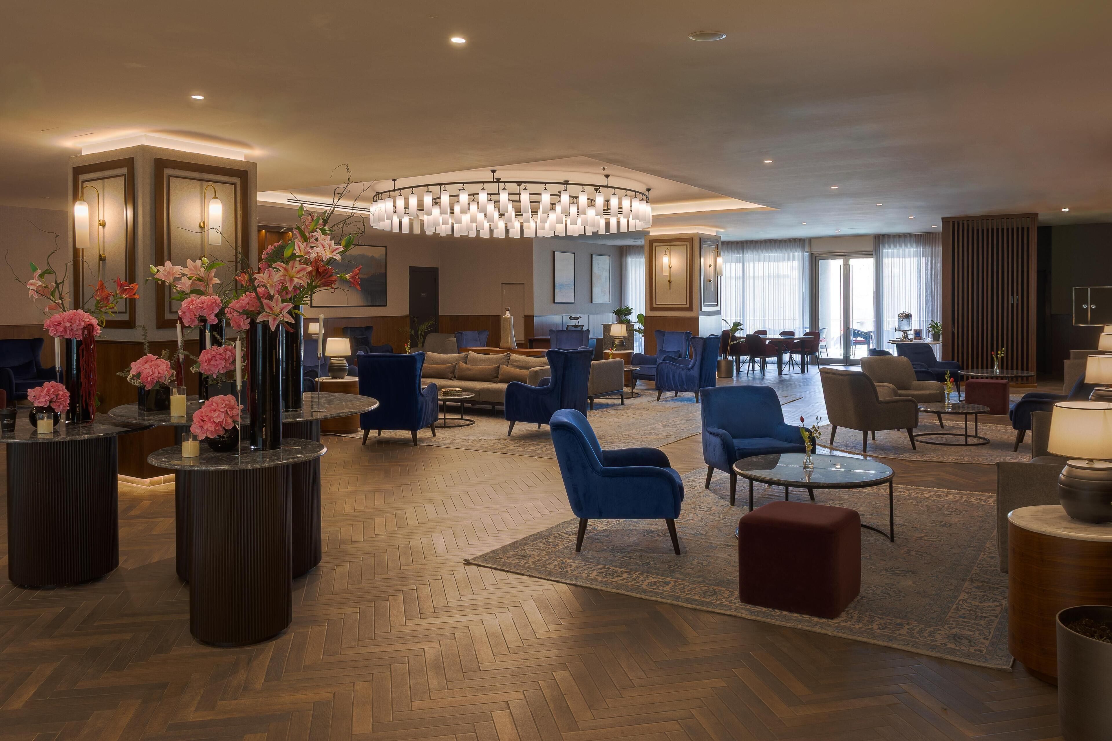 A spacious lobby with modern furniture, a large chandelier, and decorative vases with flowers.