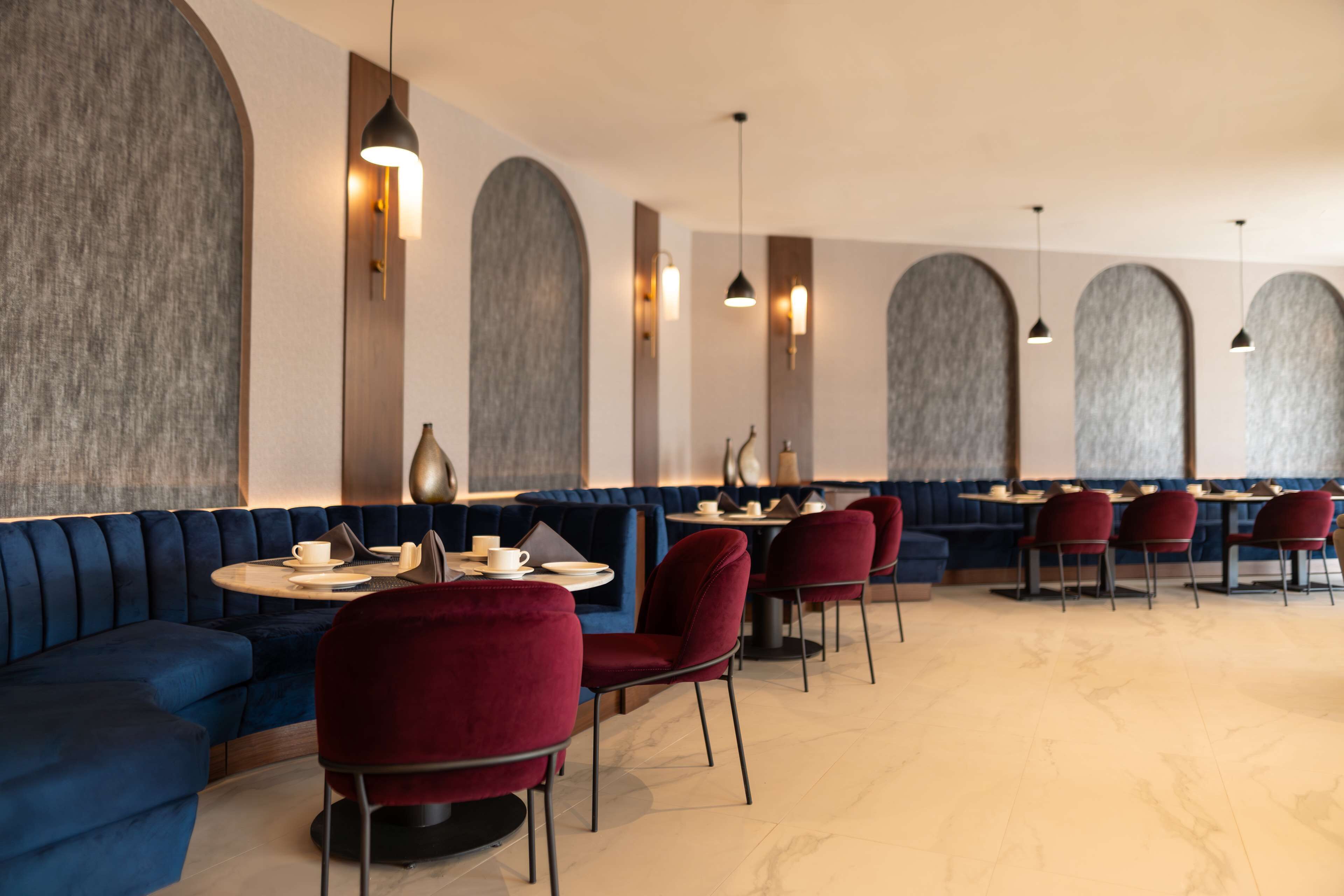 A modern restaurant with blue upholstered seating, red chairs, and round tables.
