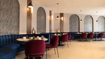 A modern restaurant with blue upholstered seating, red chairs, and round tables.