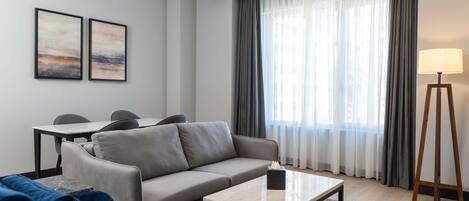 Una sala de estar moderna con sofá, una mesa de centro, una lámpara y un comedor con sillas.