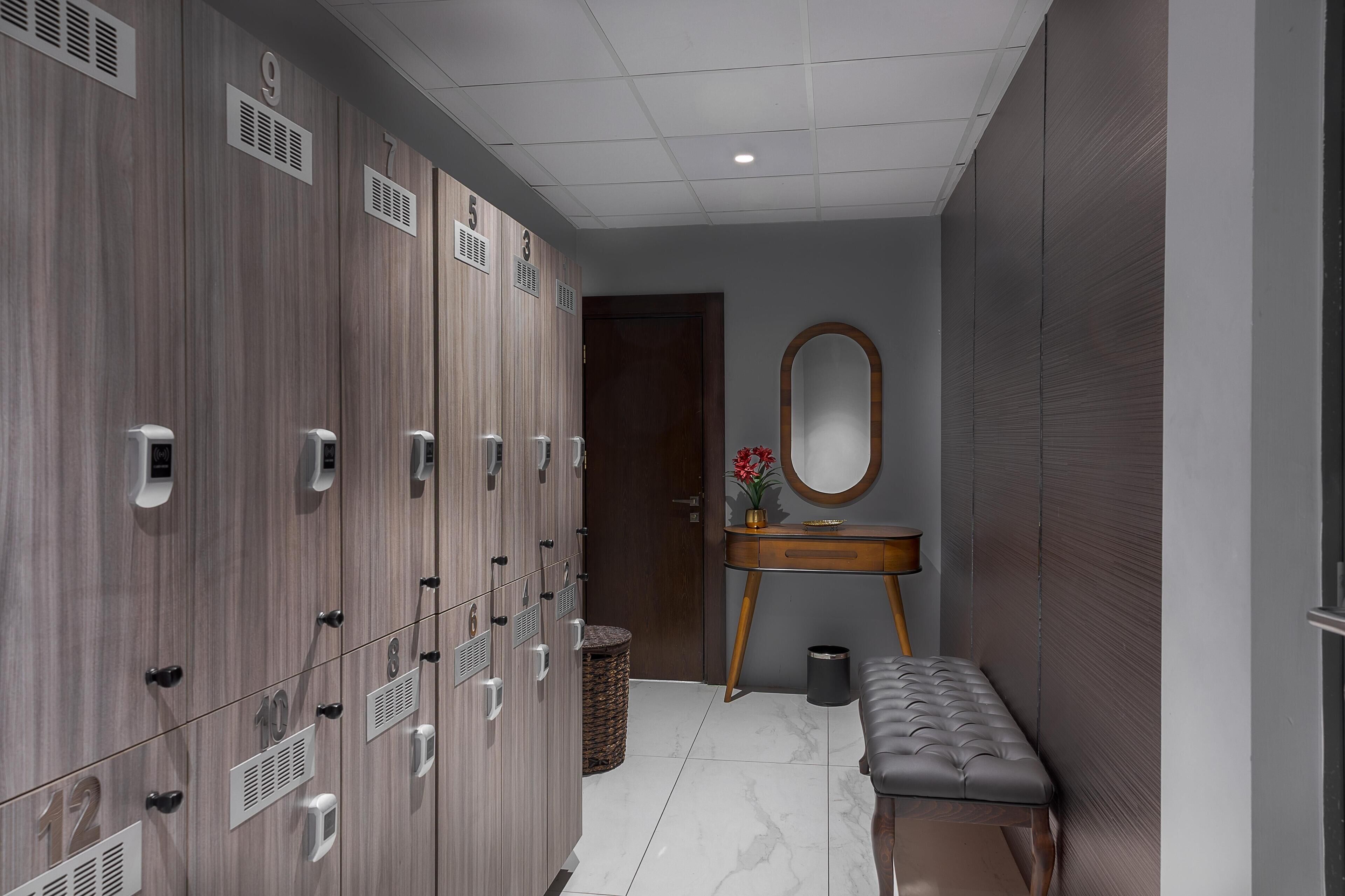 A locker room with numbered lockers, a bench, a mirror, and a trash bin.