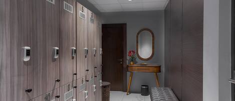A locker room with numbered lockers, a bench, a mirror, and a trash bin.