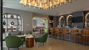 A modern bar area with a sleek bar counter, green upholstered chairs, and a well-lit ceiling with geometric light fixtures. - Radisson Blu Hotel, Amman Galleria Mall (Amman)