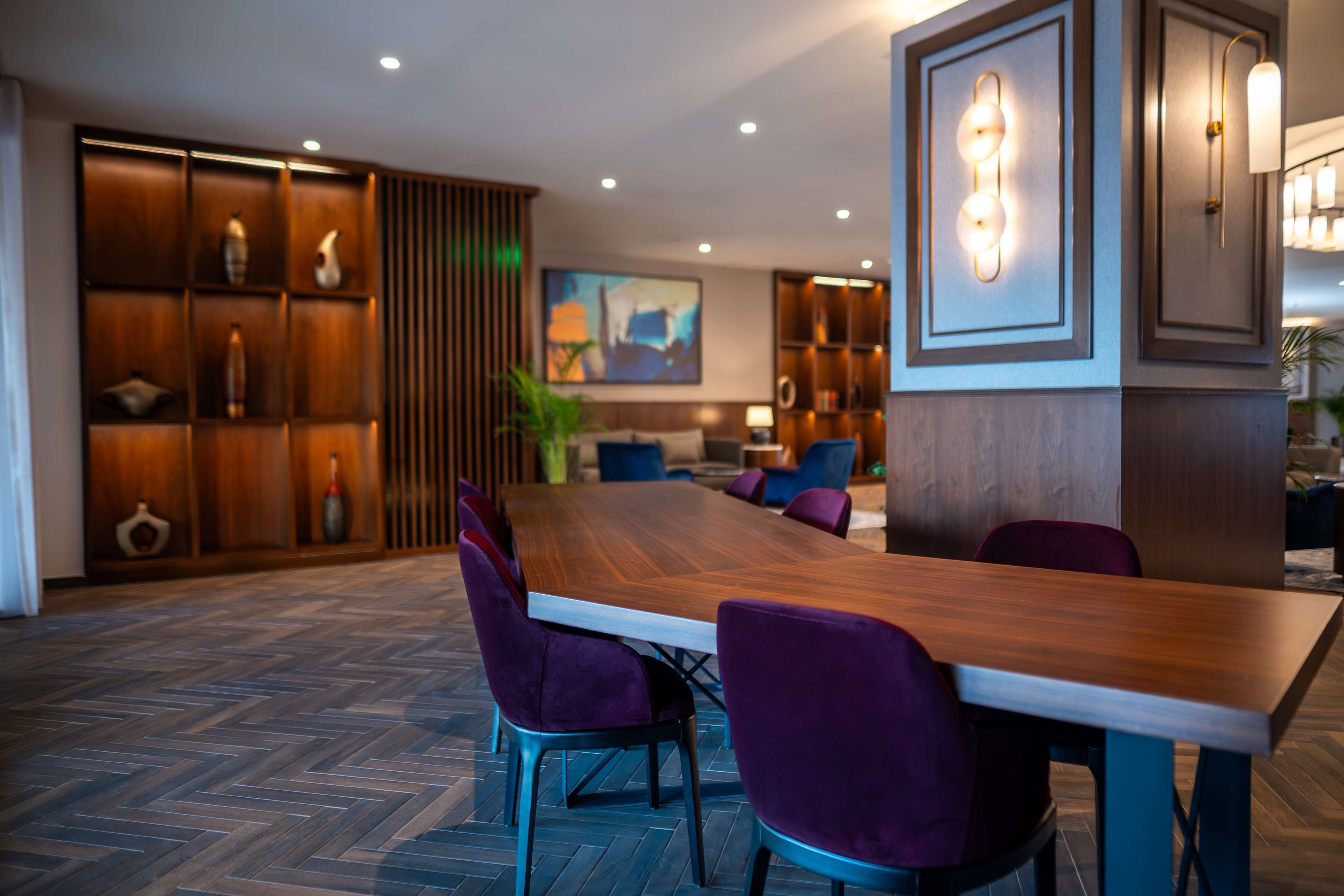 A spacious dining area with a long wooden table and purple upholstered chairs, surrounded by wooden paneling and recessed lighting.