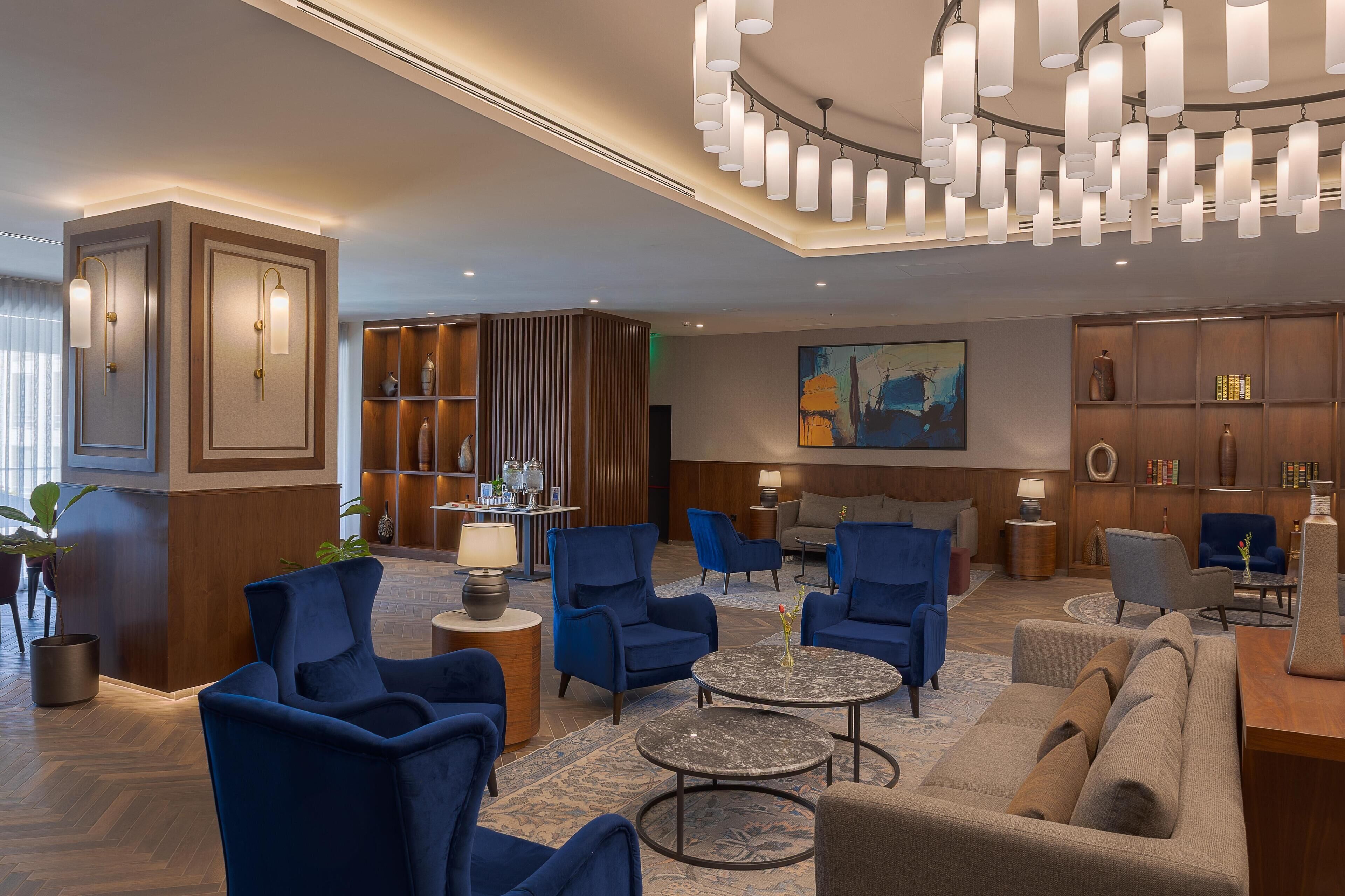 A modern lobby with blue armchairs, a round coffee table, and a chandelier.