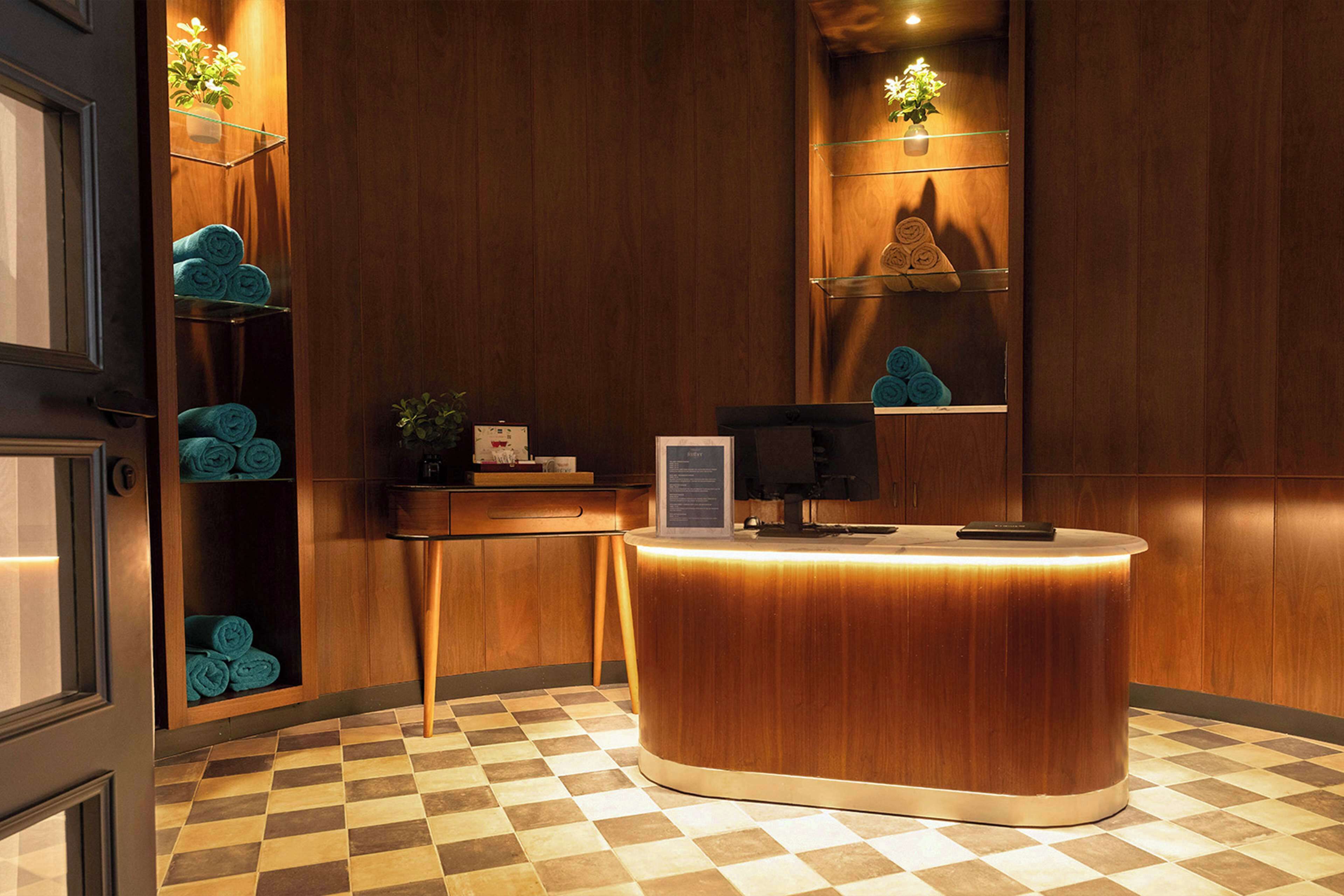 Zona de recepción con mostrador de madera, área de registro y estantes con toallas enrolladas.