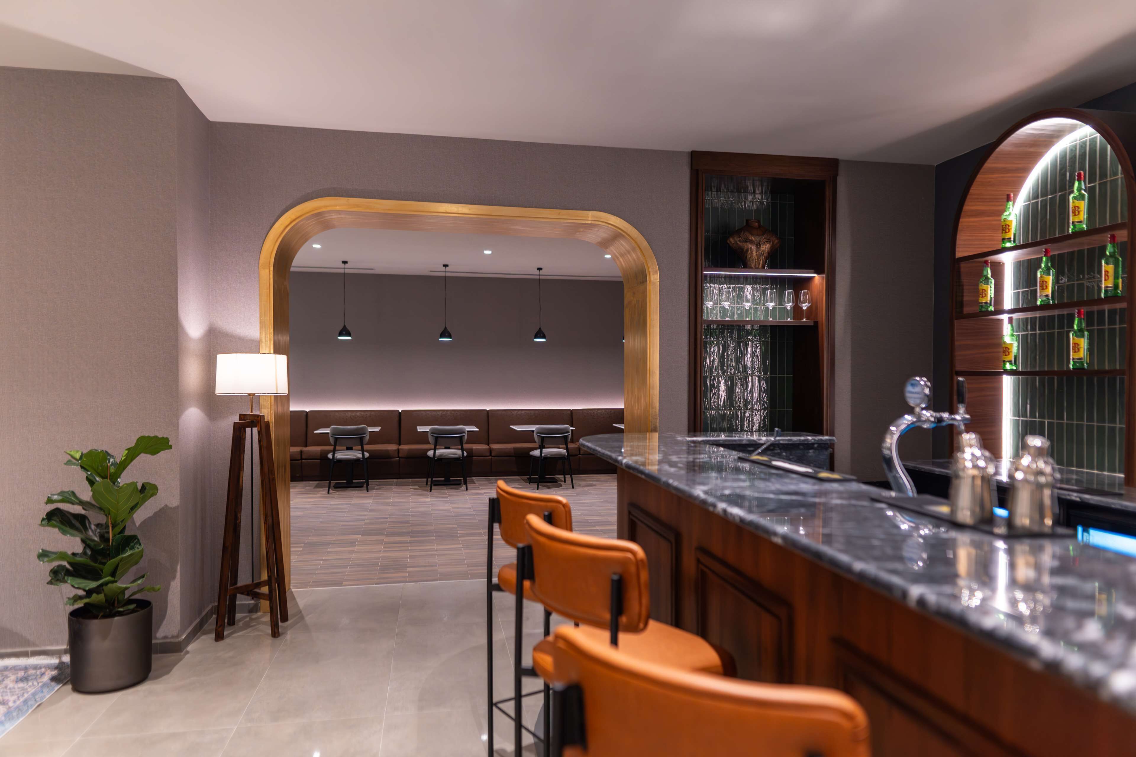 A modern bar area with a marble countertop, bar stools, and a seating area with tables and chairs.