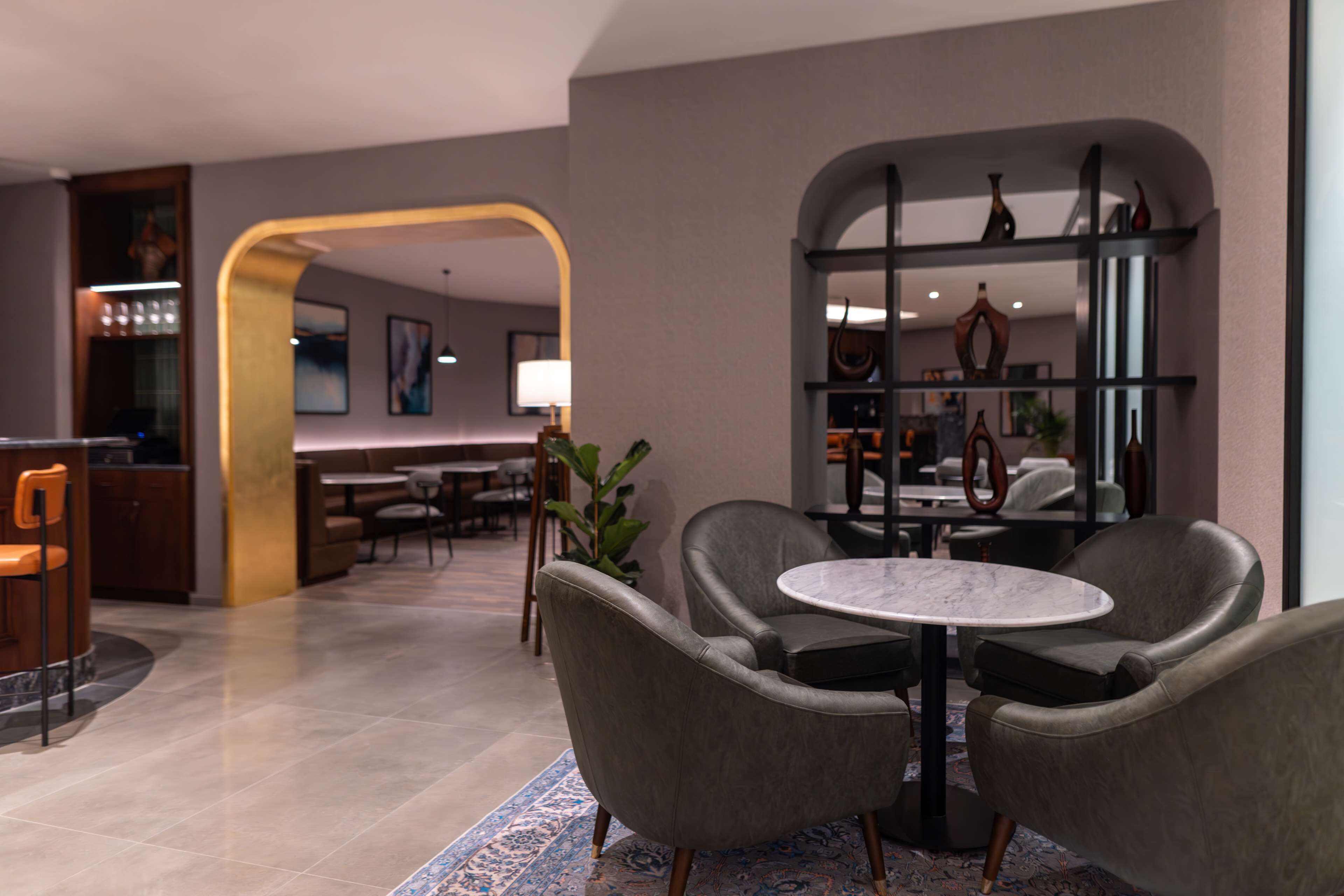 Un moderno vestíbulo de hotel con sillones de cuero, una mesa de mármol y un arco central.