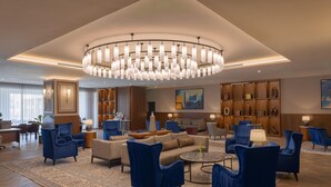 A spacious lobby with a large chandelier, blue armchairs, a sofa, and a coffee table. There are bookshelves and a painting on the walls. - Radisson Blu Hotel, Amman Galleria Mall (Amman)