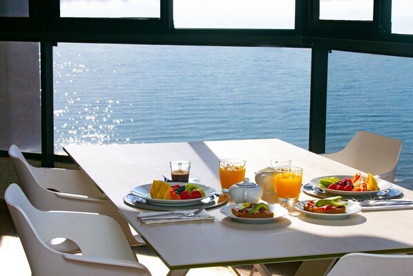 A table set with breakfast plates, glasses, and a view of the sea.