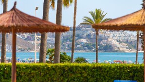 Una playa con palmeras, sombrillas y una vista de un paisaje urbano al fondo.