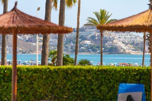Una playa con palmeras, sombrillas y una vista de un paisaje urbano al fondo.
