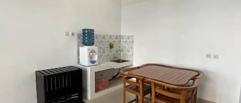 Una habitación pequeña y limpia con kitchenette, una mesa de madera con cuatro sillas, un radiador negro y un tendedero de metal.