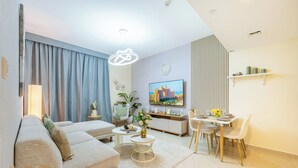 En moderne stue med sofa, sofabord, spisebord og stole. Der er et fjernsyn ophængt på væggen og en plante på sofabordet.
