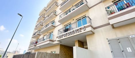 A multi-story residential building with balconies, a sign indicating 'May Residence 5', and an emergency exit sign.