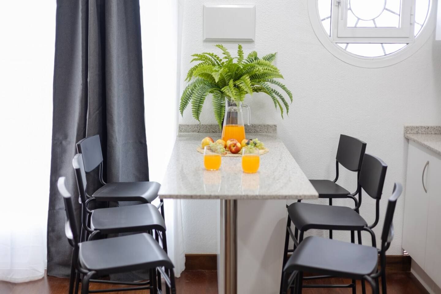 Een eethoek met een tafel gedekt voor vier personen, een bloempot en fruit en sap op tafel.