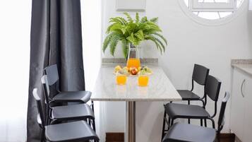 Een eethoek met een tafel gedekt voor vier personen, een bloempot en fruit en sap op tafel.