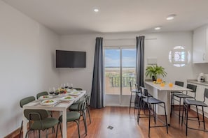 A dining area with a table set for four, a television mounted on the wall, and a view of the outdoors through a sliding door. - Coral SeaShell by Fidalsa (Lomas de Polo-Pinomar)