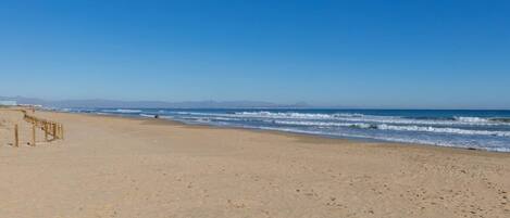 A sandy beach with a wooden walkway leading to the water, a clear sky, and distant mountains.