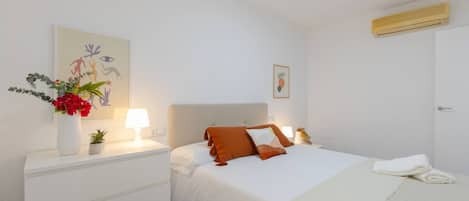 A hotel room with a bed, bedside tables, a nightstand, a wall-mounted air conditioner, and artwork on the walls.