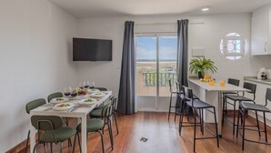 A dining area with a table set for four, a television mounted on the wall, and a balcony with a view. - Coral SeaShell by Fidalsa (Lomas de Polo-Pinomar)