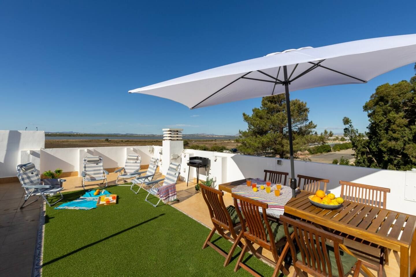En tagterrasse med et bord, stole, en stor parasol og en pool.