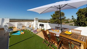 A rooftop terrace with a table, chairs, a large umbrella, and a pool.