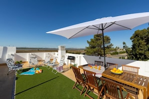 Una terraza en la azotea con una mesa, sillas, una sombrilla grande y una piscina.