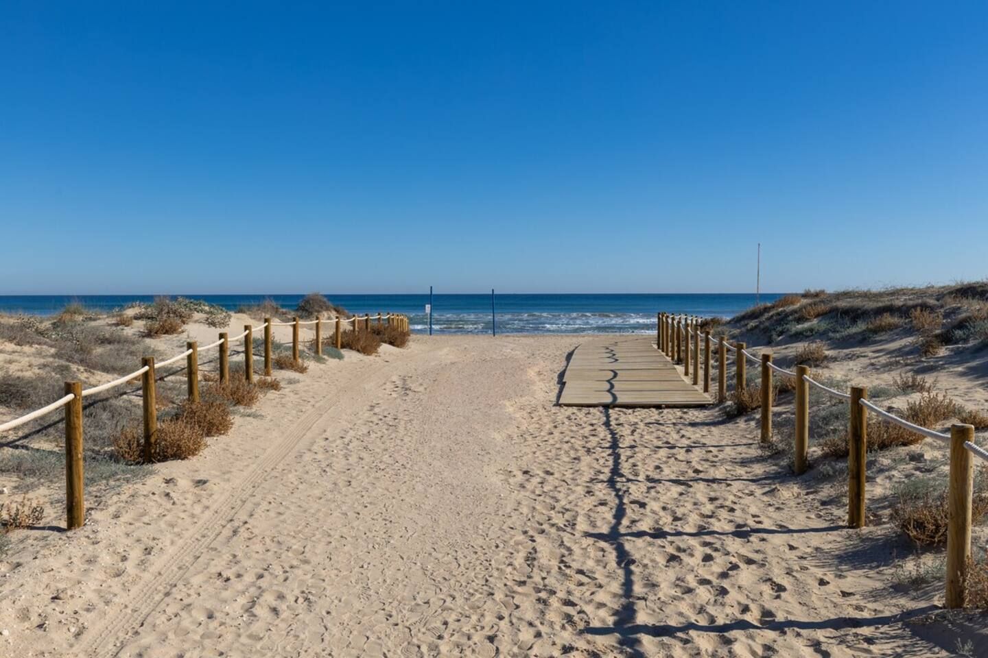 Een zandpad langs het strand dat naar de oceaan leidt, met houten leuningen aan beide zijden.