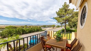 A balcony with a table and chairs, a view of a road and trees, and a distant landscape.