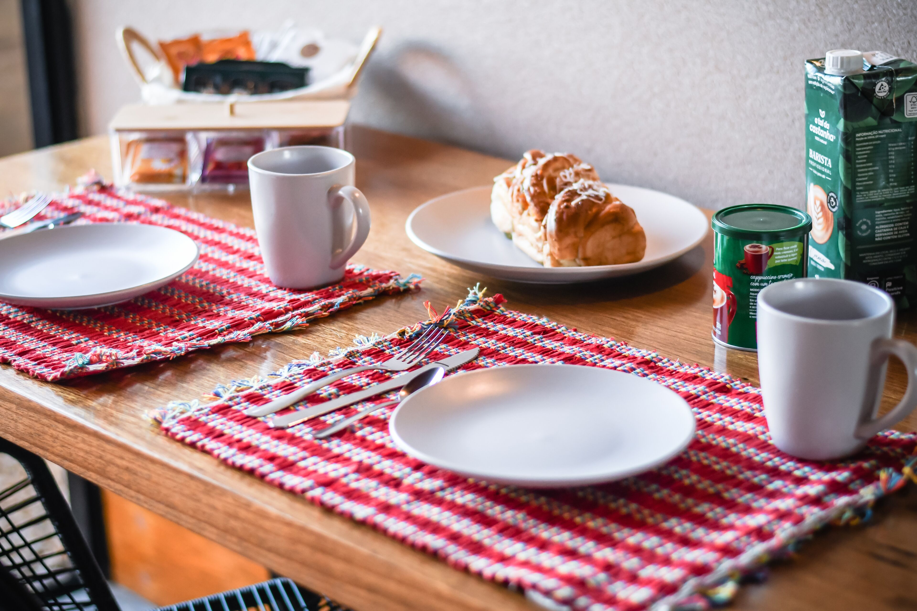 A breakfast setting with a croissant, coffee, and a carton of milk on a wooden table.