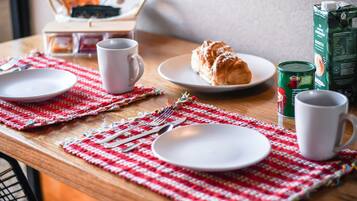 Un desayuno con un croissant, café y un cartón de leche sobre una mesa de madera.