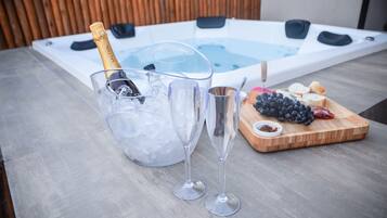 Un jacuzzi con champán y copas sobre una mesa, y una tabla de madera con uvas y pan.