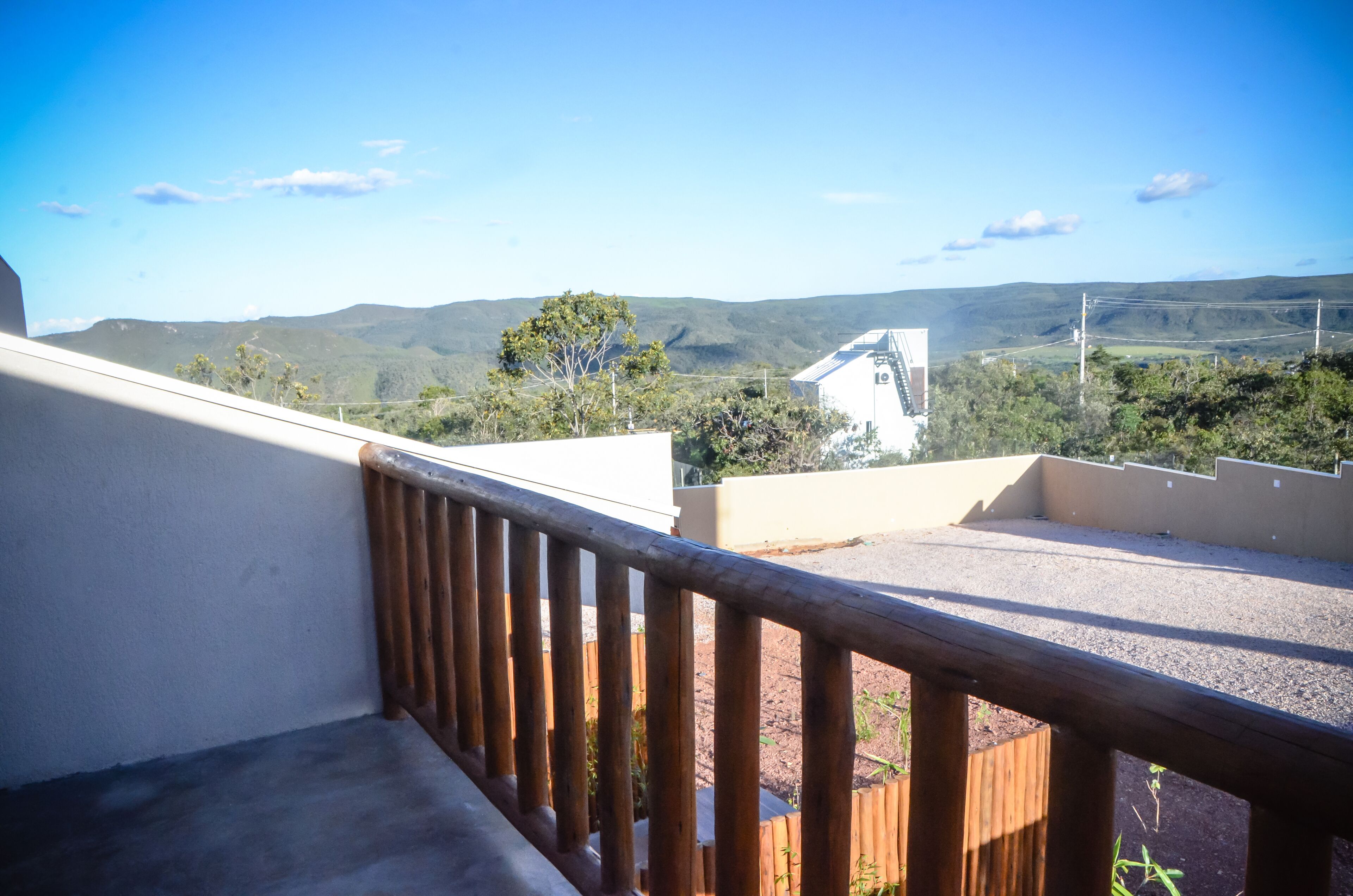 A balcony with a wooden railing overlooking a landscape with hills and a white building in the distance.