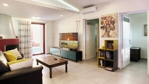 A living room with a sofa, coffee table, TV, bookshelf, and a painting on the wall.