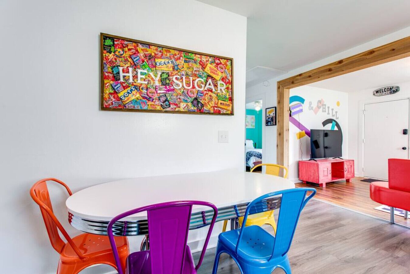 Un salon moderne avec une peinture abstraite aux couleurs vives accrochée au mur, une table ronde blanche entourée de chaises colorées et un canapé rouge.
