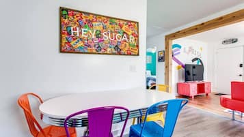 A modern living room with a colorful abstract painting on the wall, a round white table with colorful chairs, and a red sofa.