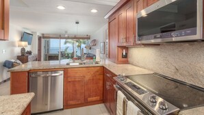 A modern kitchen with wooden cabinets, stainless steel appliances, and a large island with a built-in oven. - ENDLESS OCEAN VIEWS- PREMIUM LOCATION & FINISHES-TOP FLOOR-WELL EQUIPPED (Kihei)
