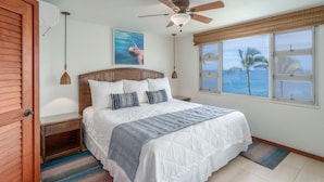 A bedroom with a bed, a ceiling fan, a window with a view of the ocean, and a painting on the wall. - ENDLESS OCEAN VIEWS- PREMIUM LOCATION & FINISHES-TOP FLOOR-WELL EQUIPPED (Kihei)