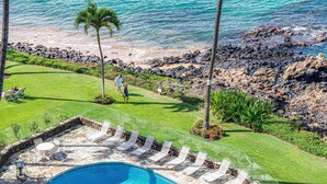 A swimming pool with lounge chairs and a stone deck, surrounded by a well-maintained lawn and a rocky shoreline. - ENDLESS OCEAN VIEWS- PREMIUM LOCATION & FINISHES-TOP FLOOR-WELL EQUIPPED (Kihei)