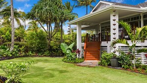 Uma casa com varanda coberta, cercada por vegetação tropical exuberante e um gramado bem cuidado.