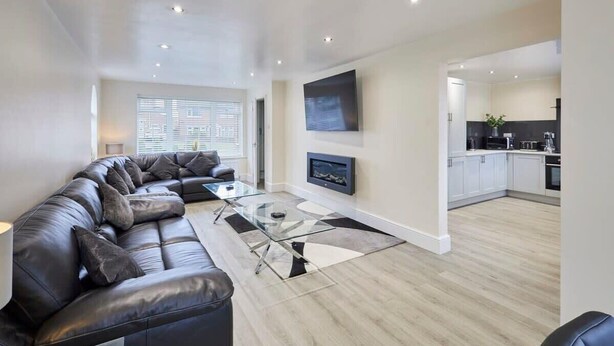 A modern living room with a leather sectional sofa, a glass coffee table, and a flat-screen TV mounted on the wall.