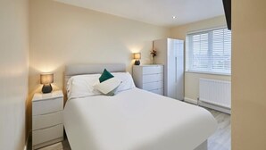 A modern bedroom with a large bed, bedside tables, a dresser, and a window with blinds.